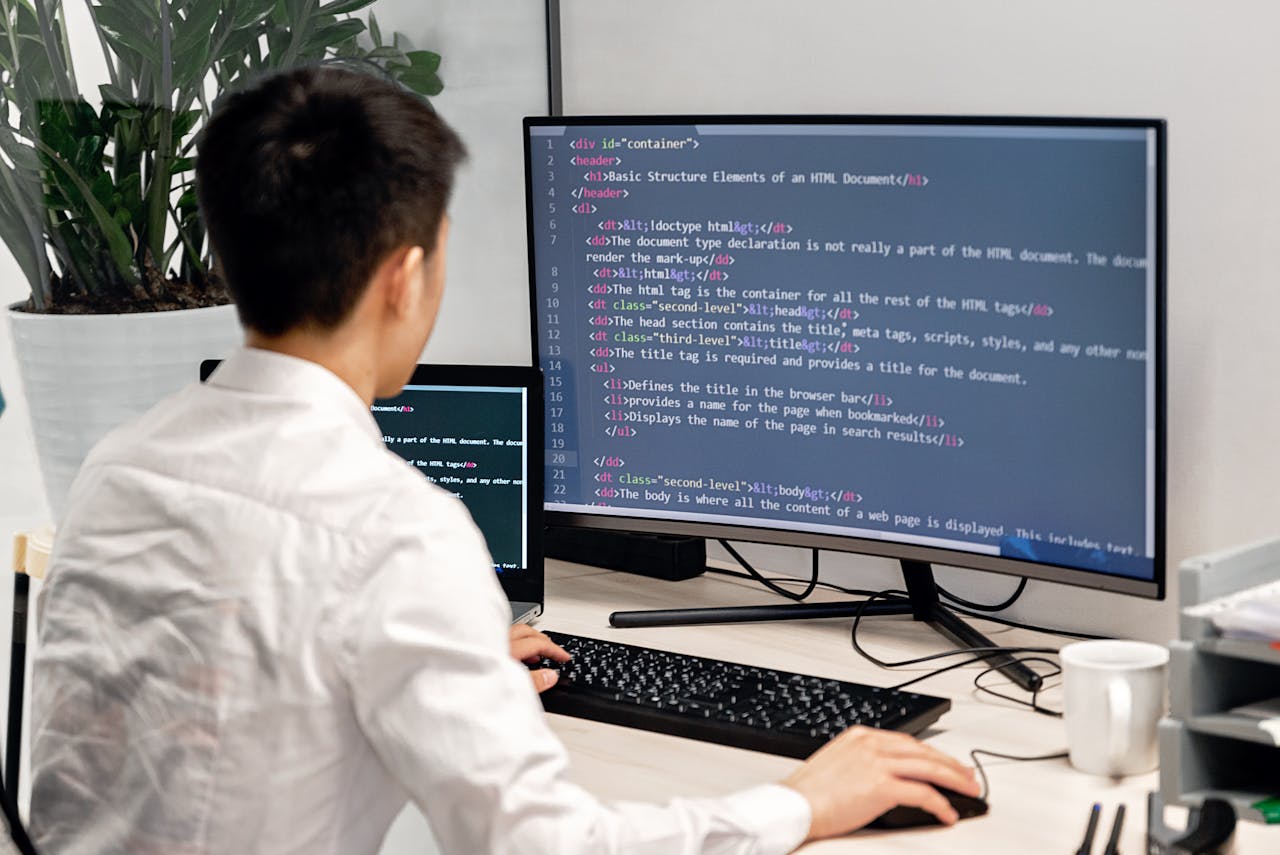 about-01 Adult male programmer coding on dual monitors in a modern indoor workspace.
